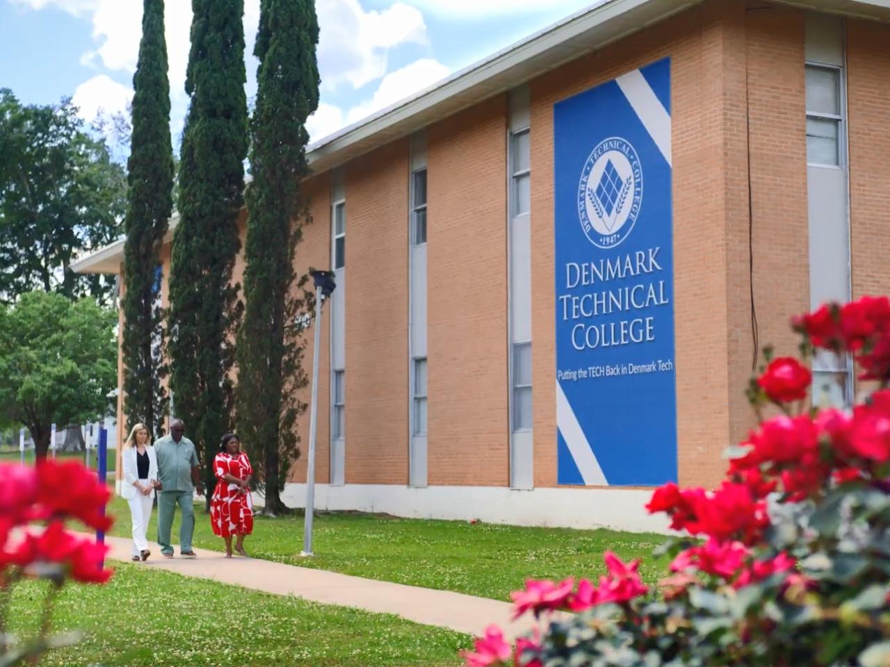 People walking down a sidewalk next to a building "Denmark Technical College" banner on the side.