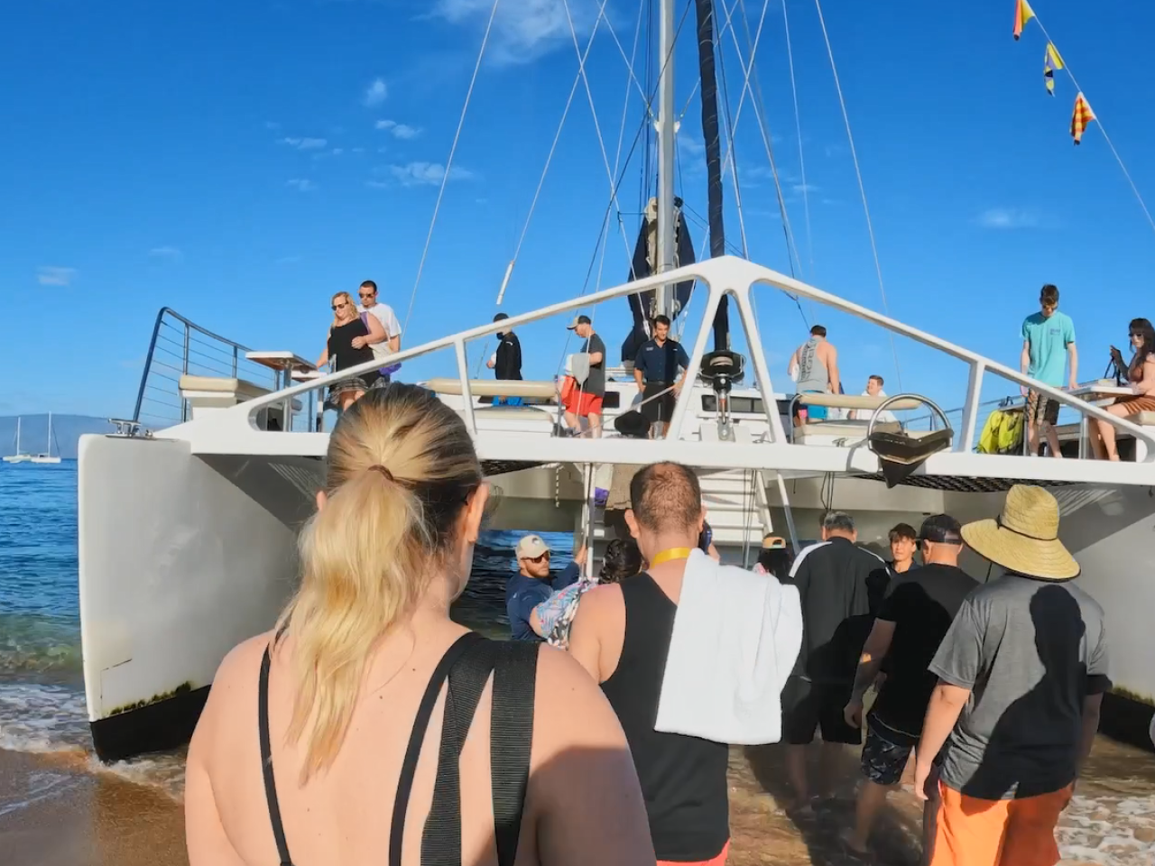 People boarding a large sail boat from a sandy shore.