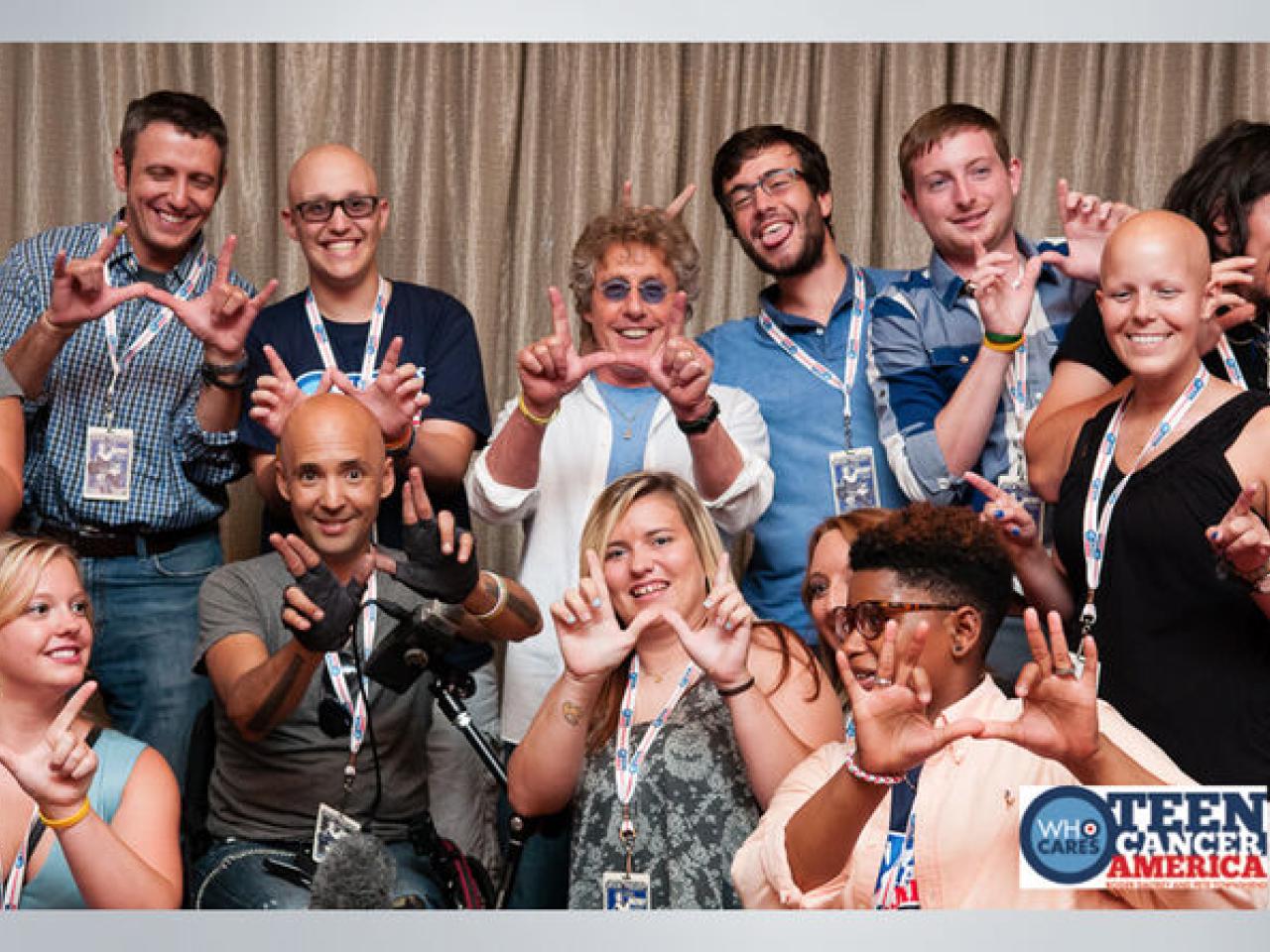 Group of 11 people stand with Roger Daltrey at the center all with their hands in the shape of a W.