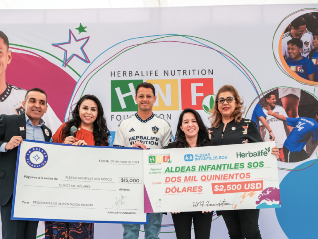 Five people in front of a large banner, holding up two checks.