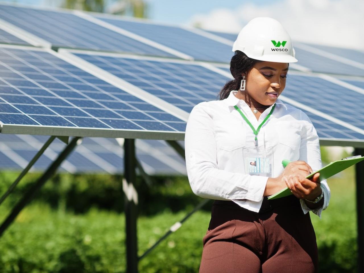 Female Wesco employee shown with a clipboard in front of a solar panel array.