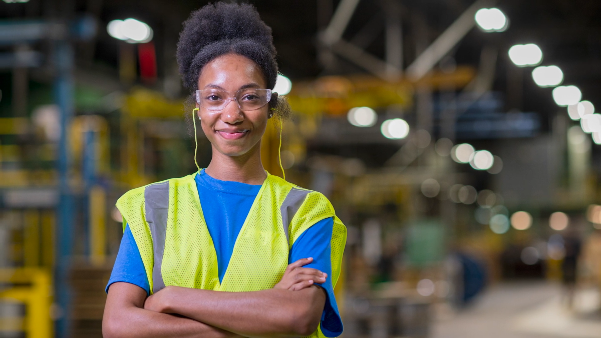 Person smiling with their arms folded, wearing safety glasses and a hi-vis vest