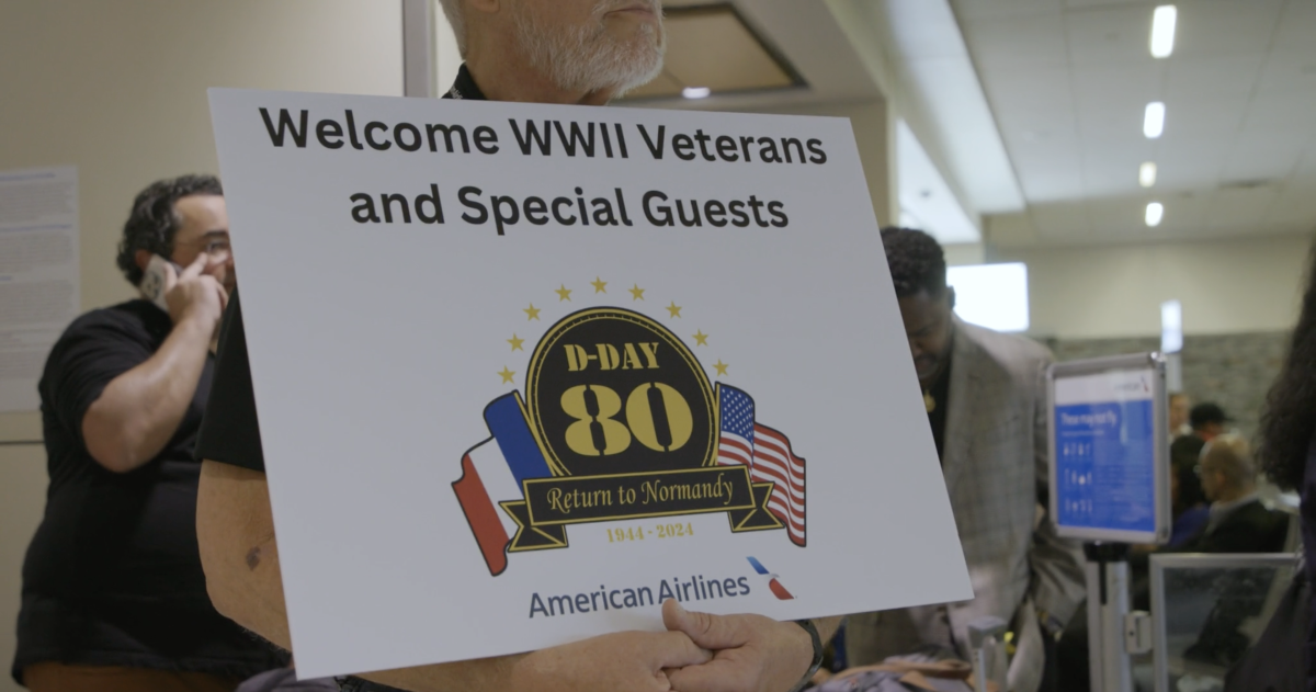 A person holding a sign that reads "Welcome WWII Veterans and Special Guests"