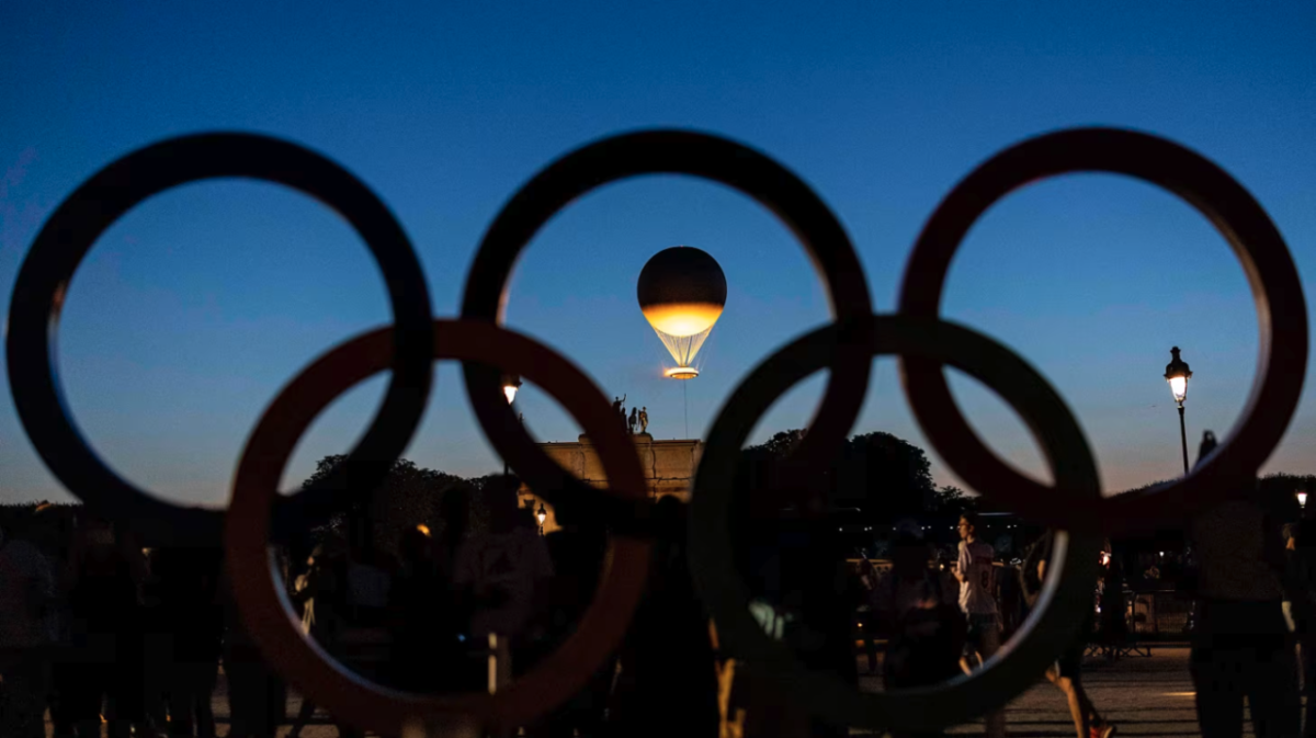 Olympic rings in silhouette with a lit balloon in the center