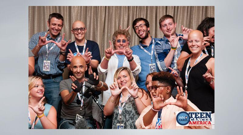 Group of 11 people stand with Roger Daltrey at the center all with their hands in the shape of a W.