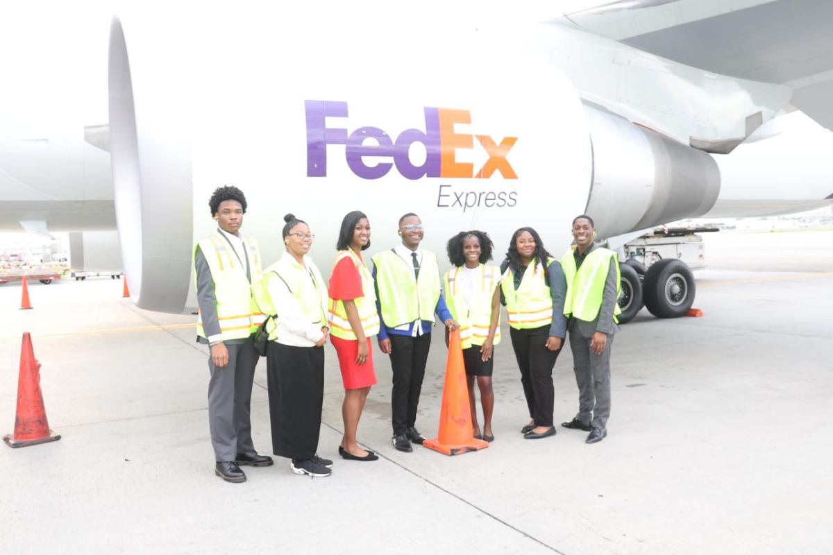 A group of people wearing hi-viz vests while stood next to a FedEx Express aeroplane 