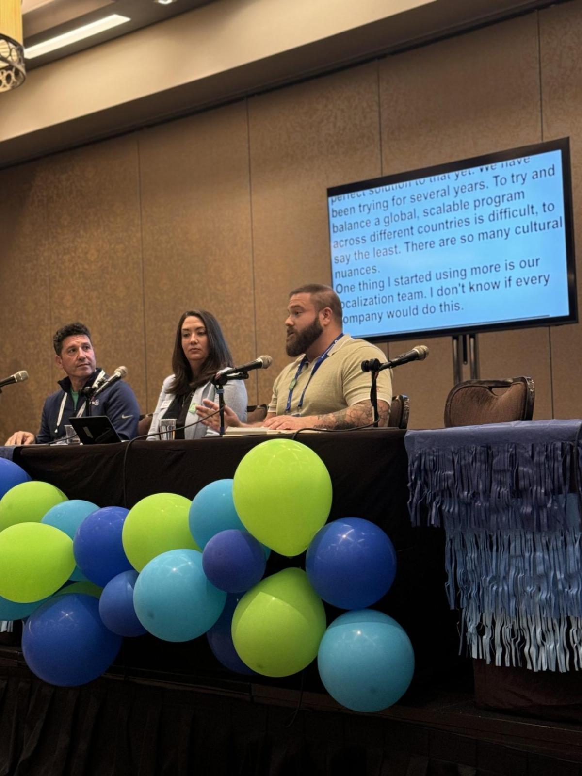 Panelists sat at a table that has green and blue balloon attached to the front 