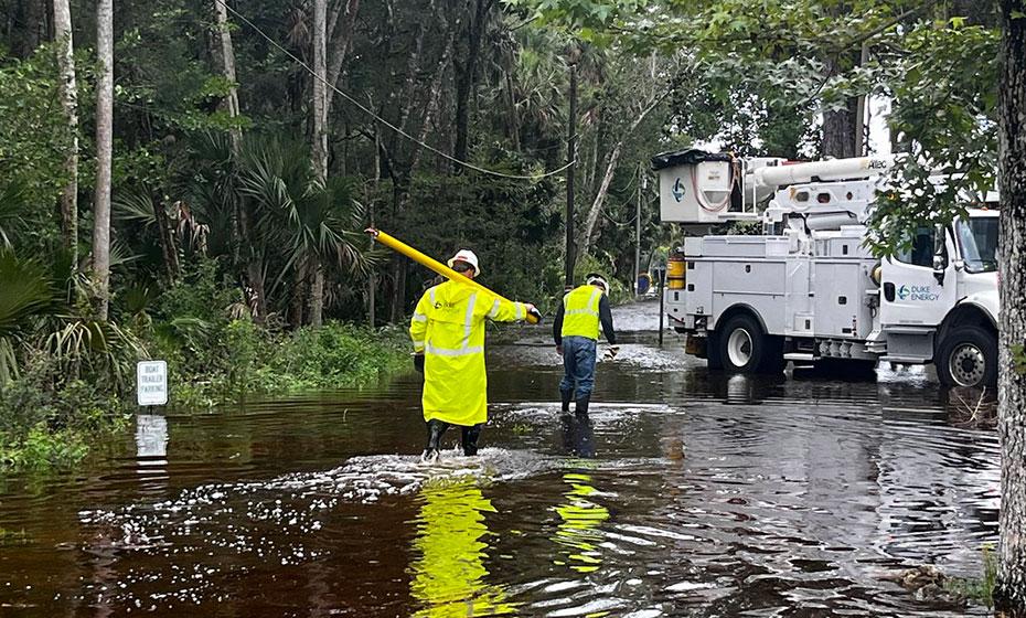 Workers in reflective jackets wading through water on a road