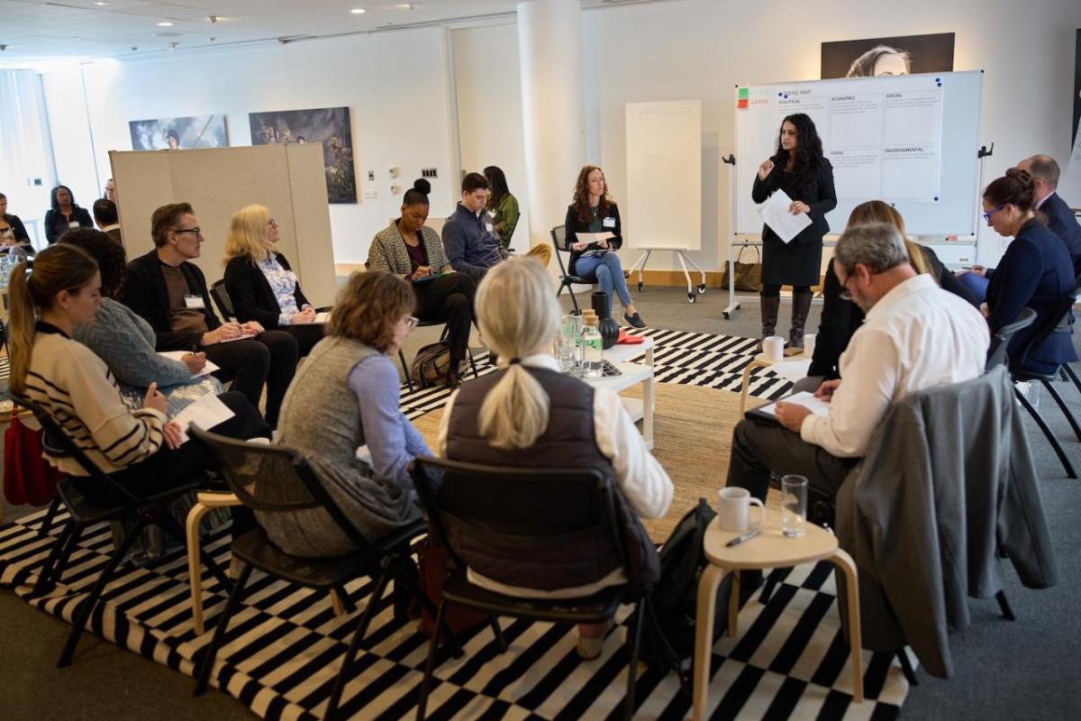 People sitting in a circle listening to someone giving a presentation