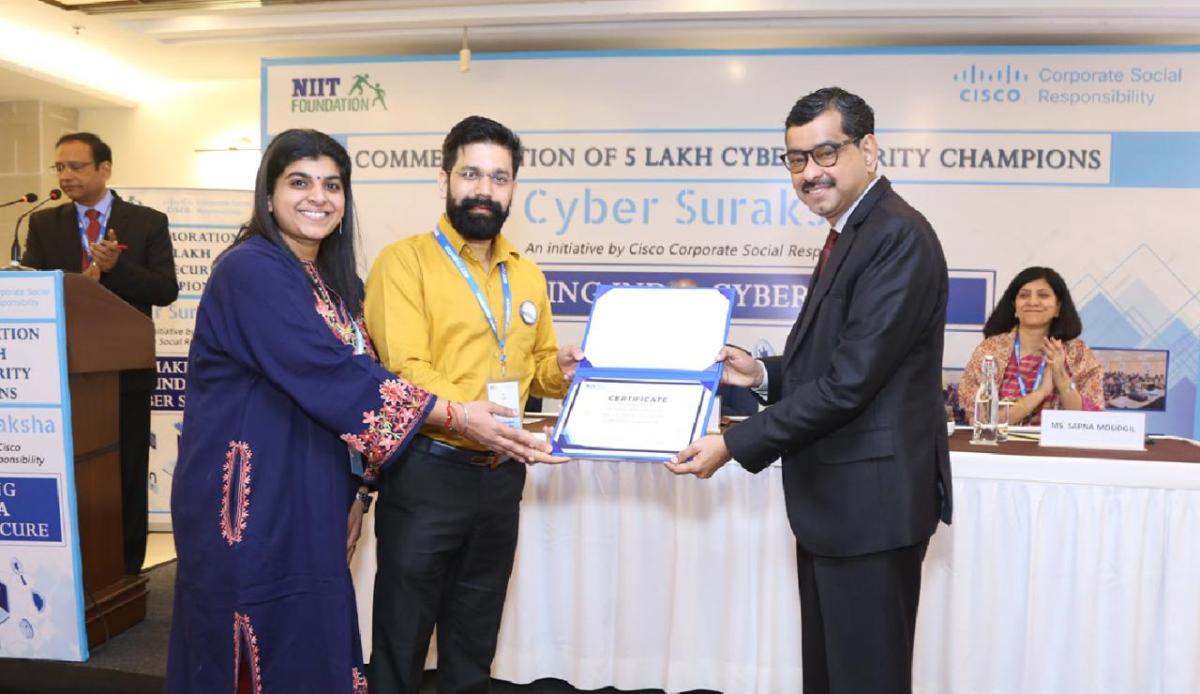 Three smiling people holding an award certificate. Others behind them.