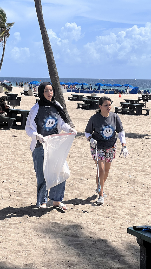 Two people in Motorola t-shirts picking up trash on a beach