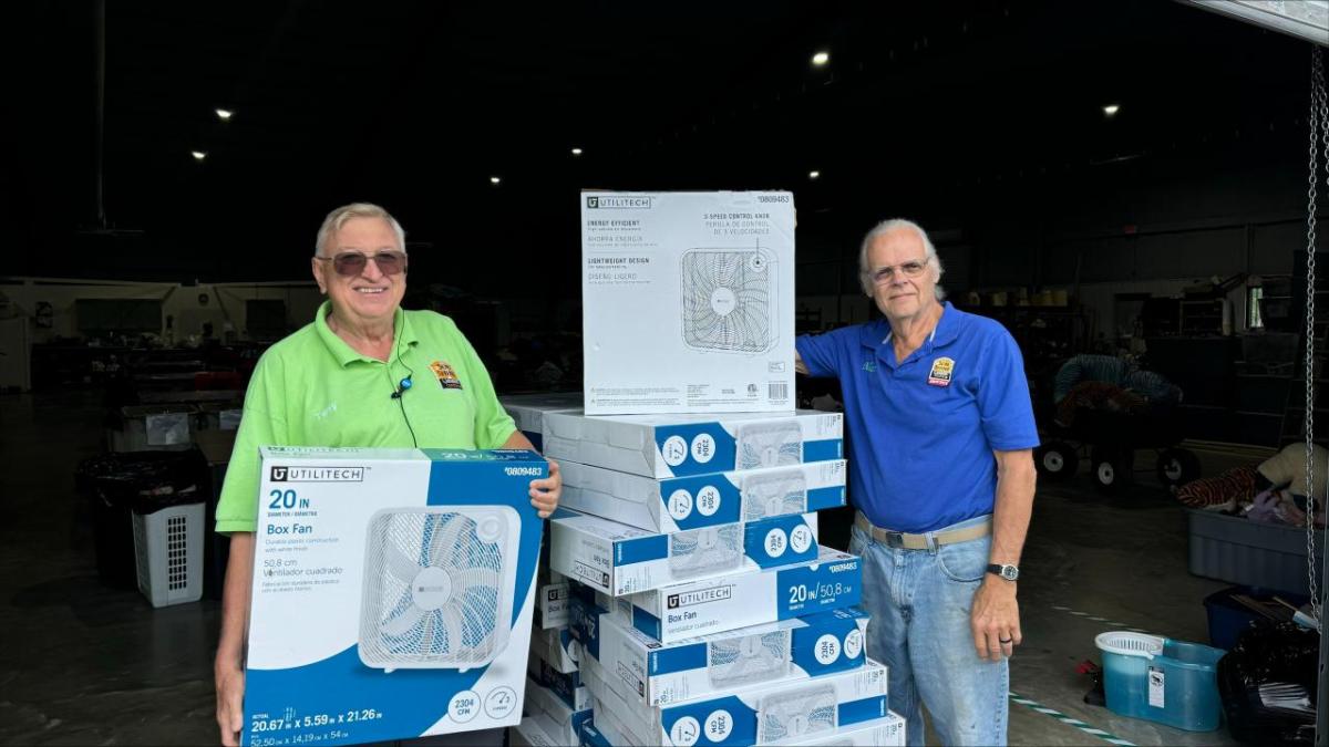 People standing next to stacks of new fans in boxes