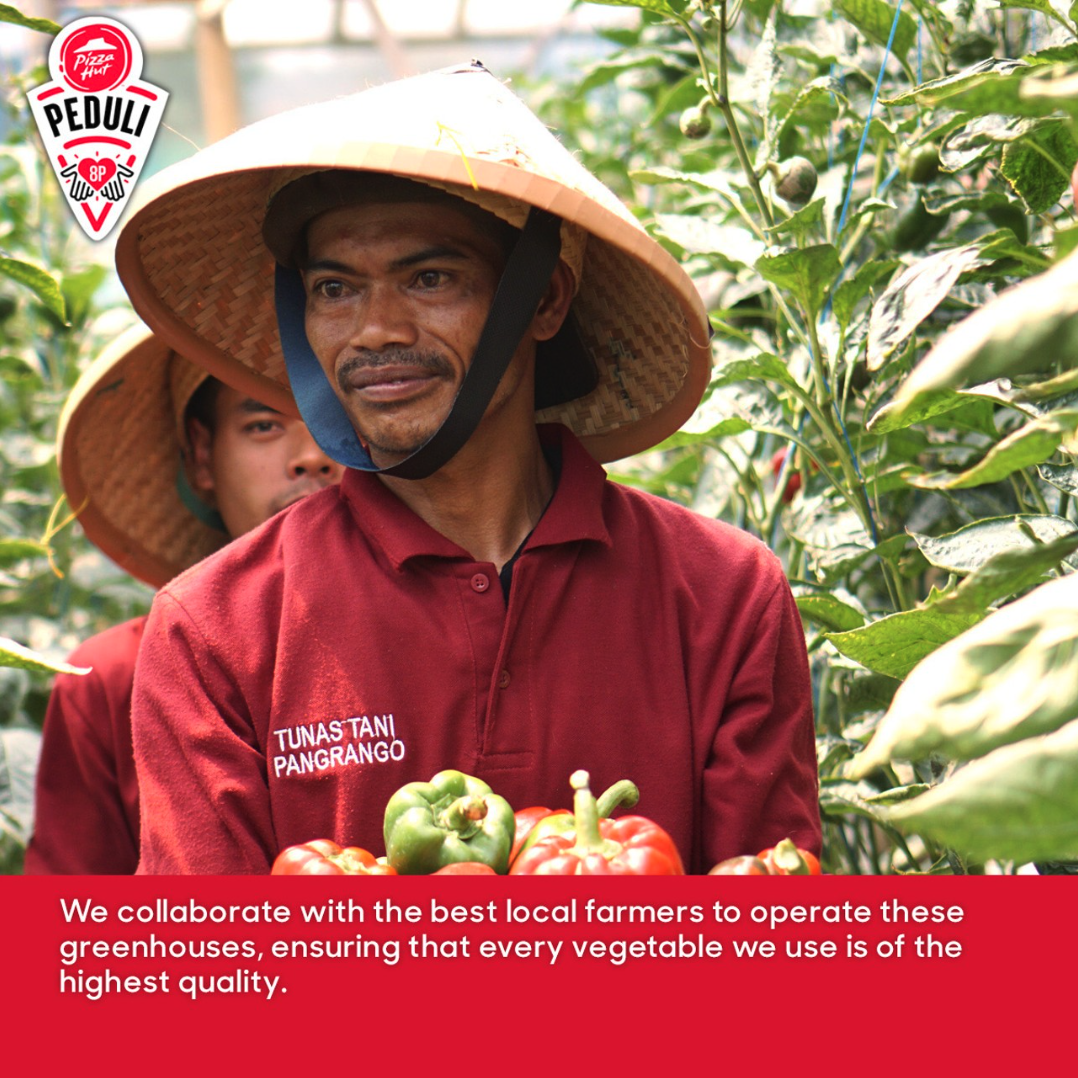 Two people holding peppers inside a greenhouse