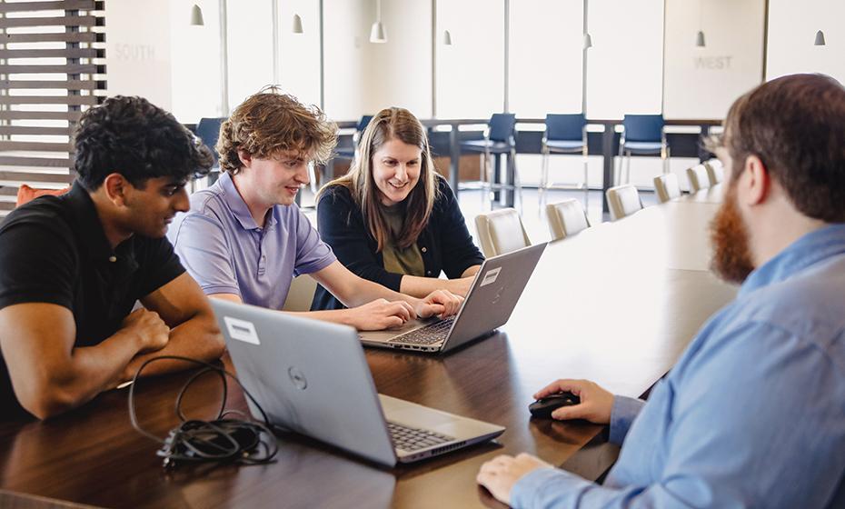 Four people at a conference table working on laptops