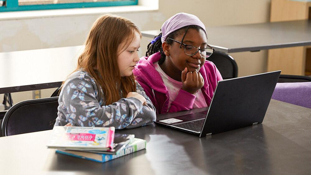 Two children sat at a desk looking at a laptop