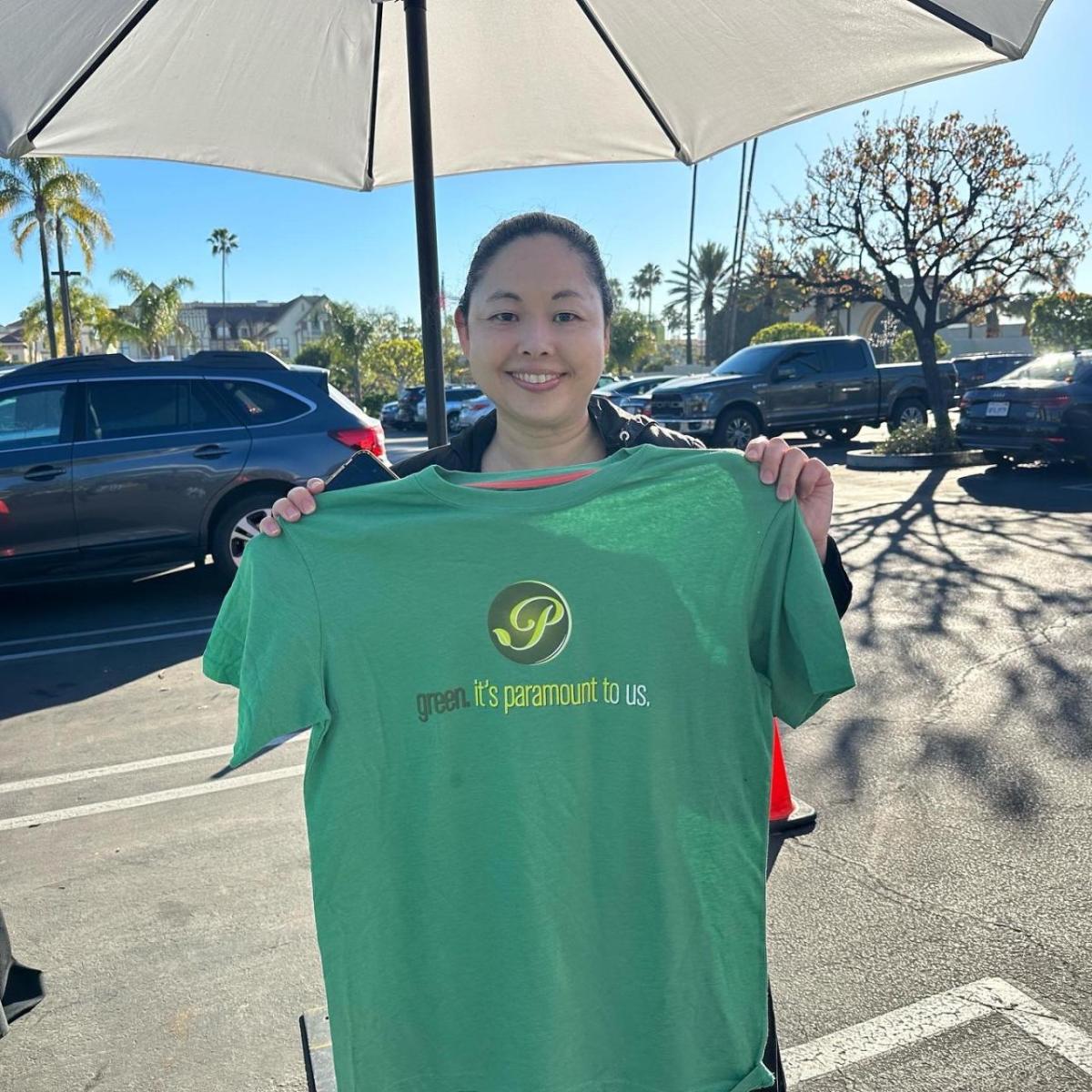 Woman holding green t-shirt that says, "Green - it's Paramount to us."