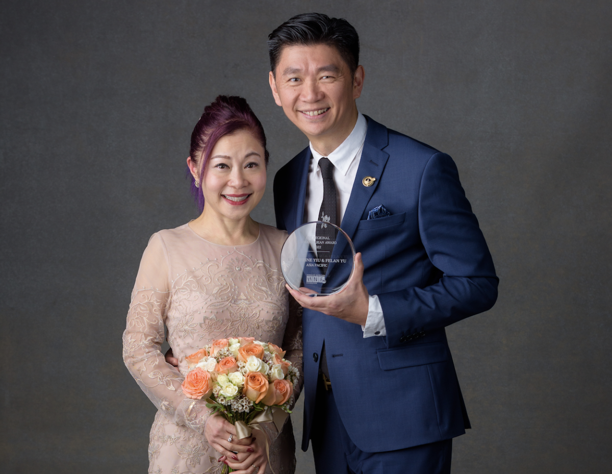 Two people stood next to each other smiling, one person holding flowers and the other holding an award