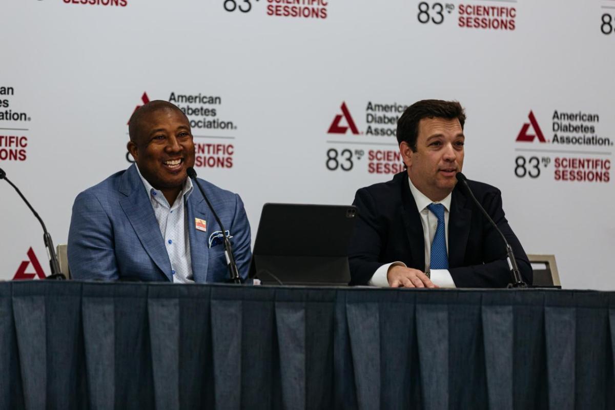 Two people seated at a table with microphones in front of backdrop with American Diabetes Association logo