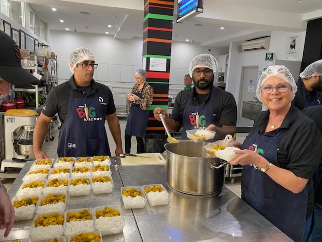 Group of volunteers in a kitchen, wearing hair nets and aprons with "Big Kitchen" on them.