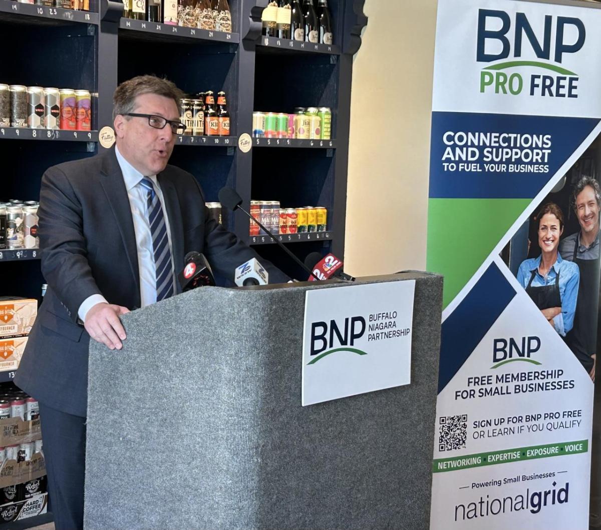 A person stood giving a speech in front of product shelves  