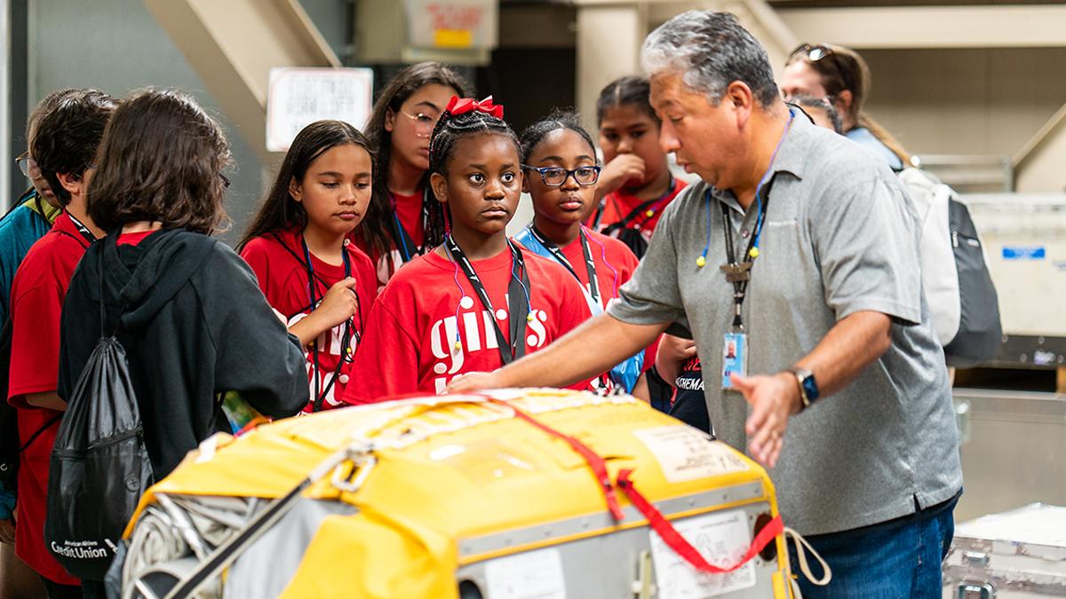 An adult showing a group of children an airplane part.