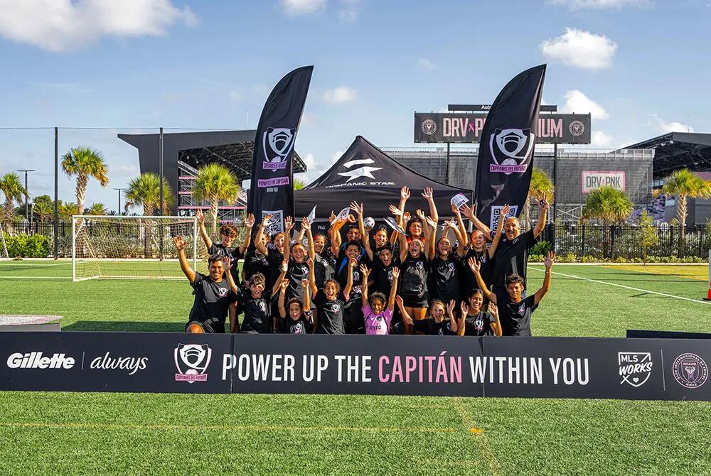 A soccer team posing with arms raised. Team banners in front and back sides "Power up the Capitan within you."