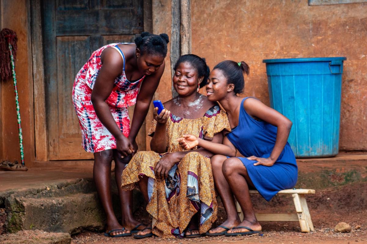 Three women in colorful dresses looking at a blue cell phone