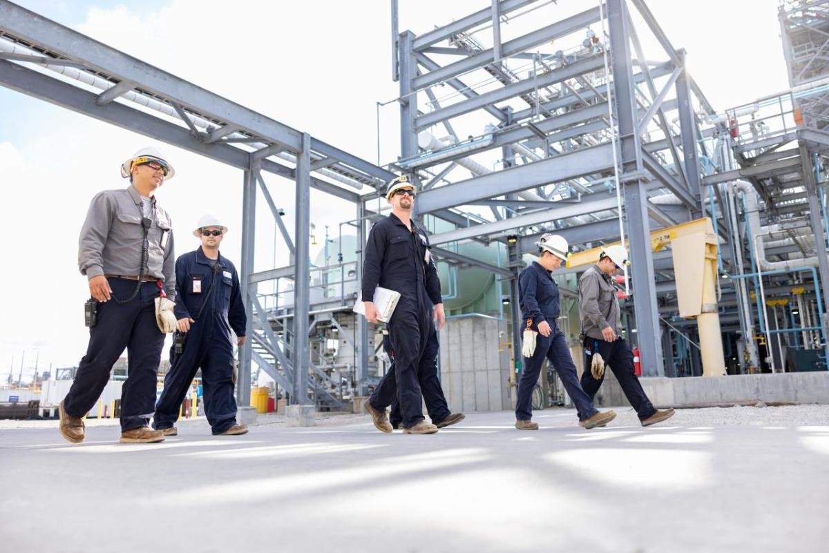 People in hard hats walking in an industrial area.