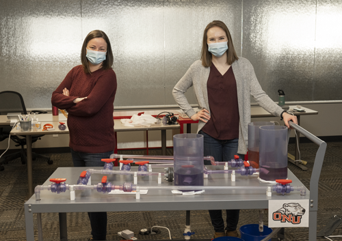 Pierce (left) and Loos (right), both graduates of ONU, pose with the ONU Model, a pipeline manifold connected to tankage.