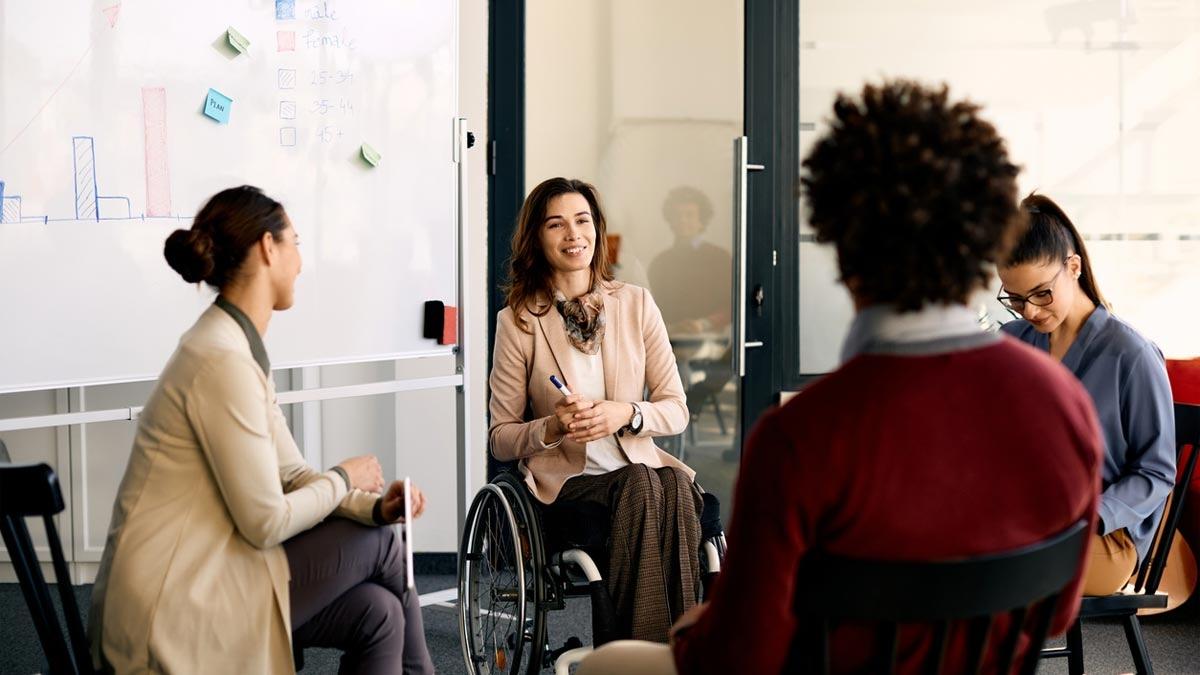 A woman is seated in a wheelchair with three coworkers.