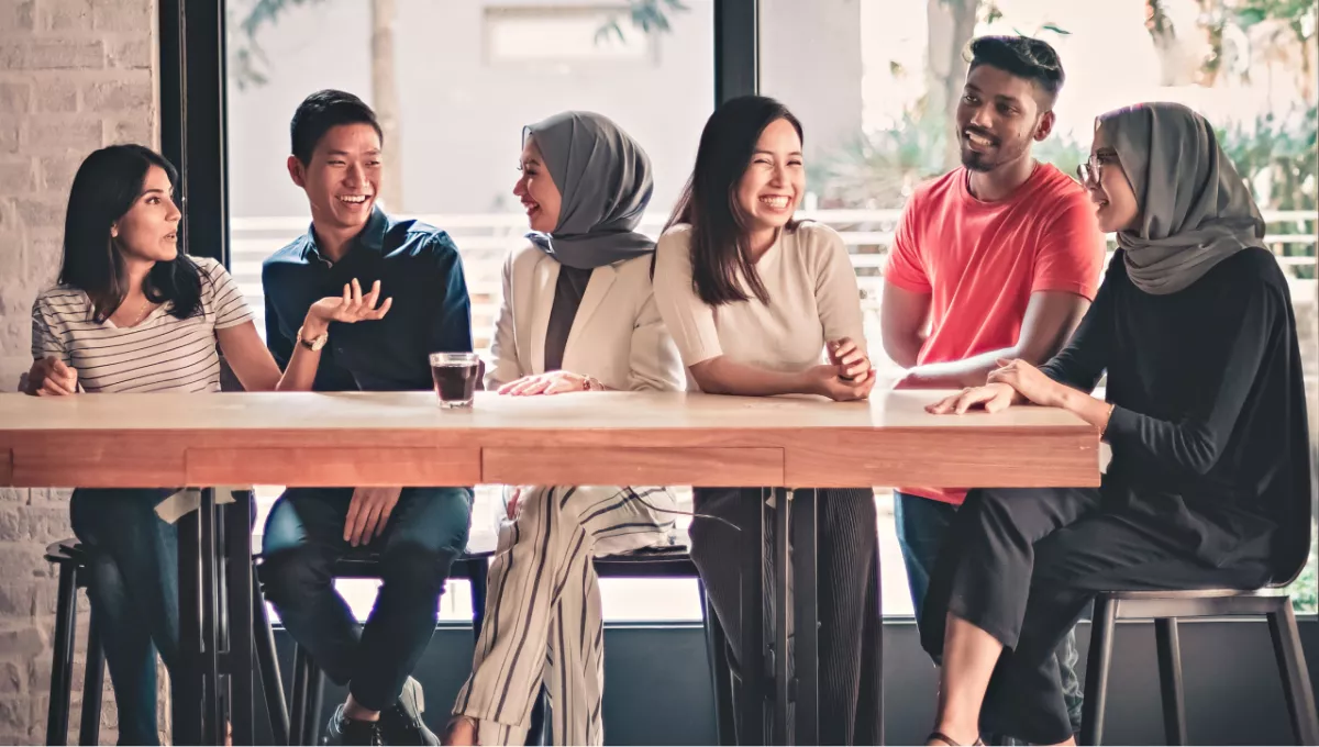 Group of six people seated at a table having coffee and smiling.