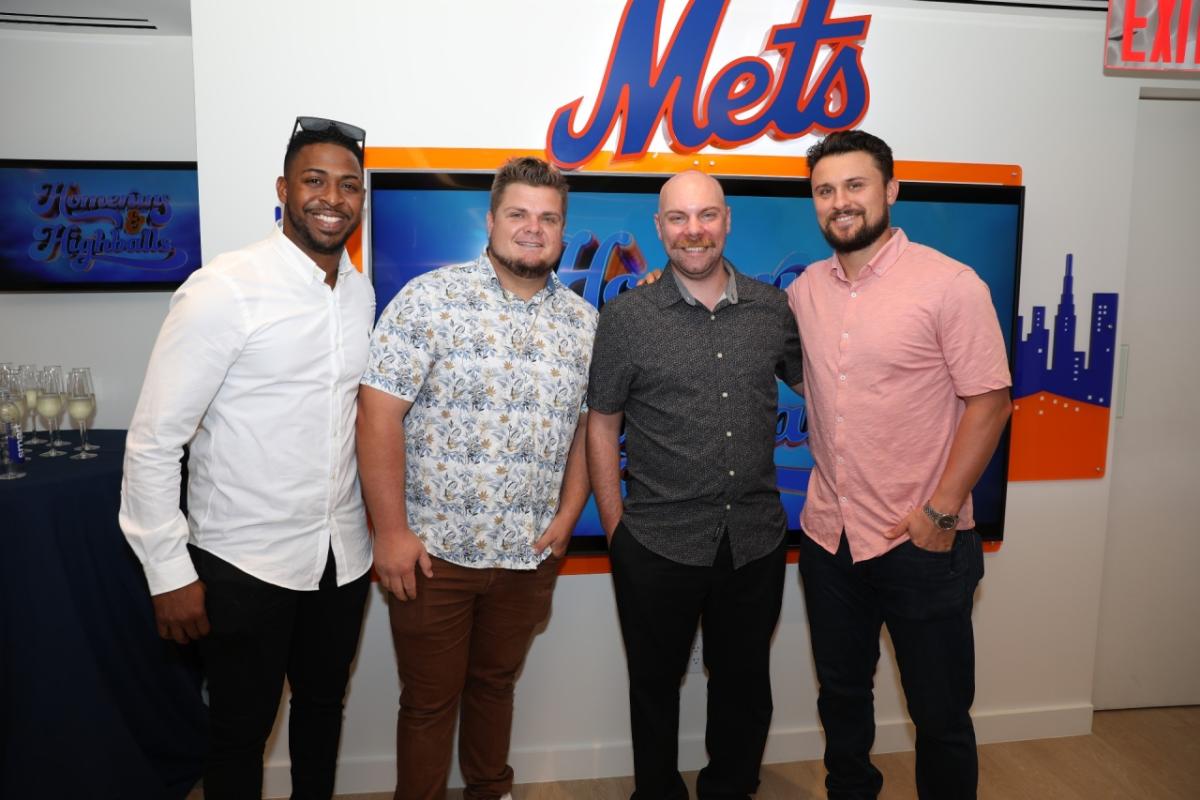 Group of four people standing in front of Mets logo