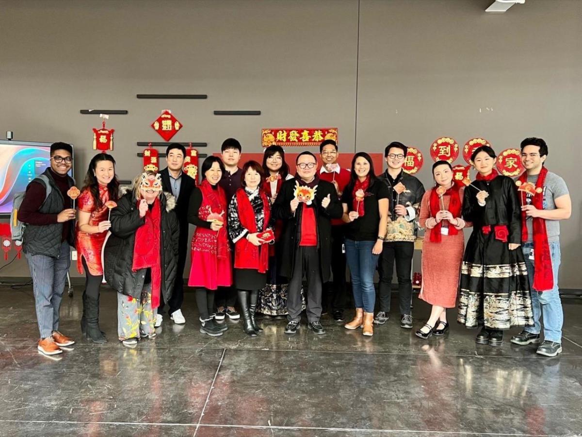 A group posed, many in matching red scarves. A display behind them.
