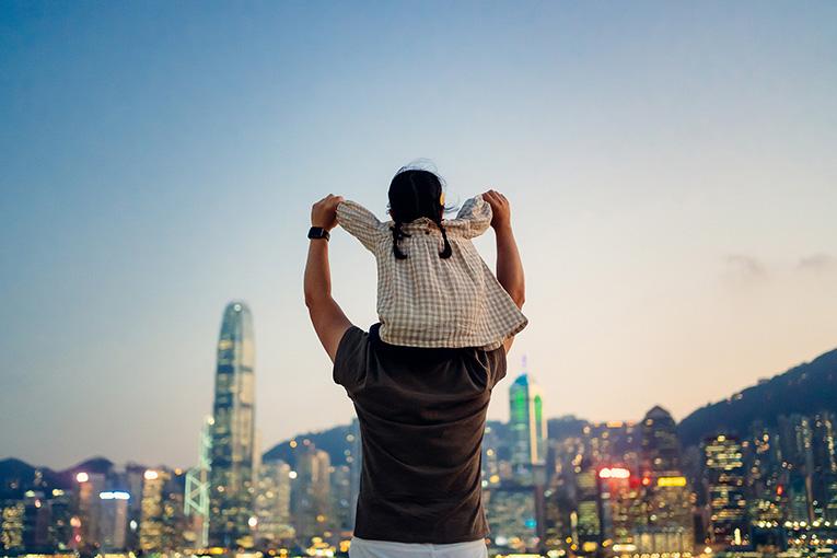 person holding small girl on shoulders in front of skyline