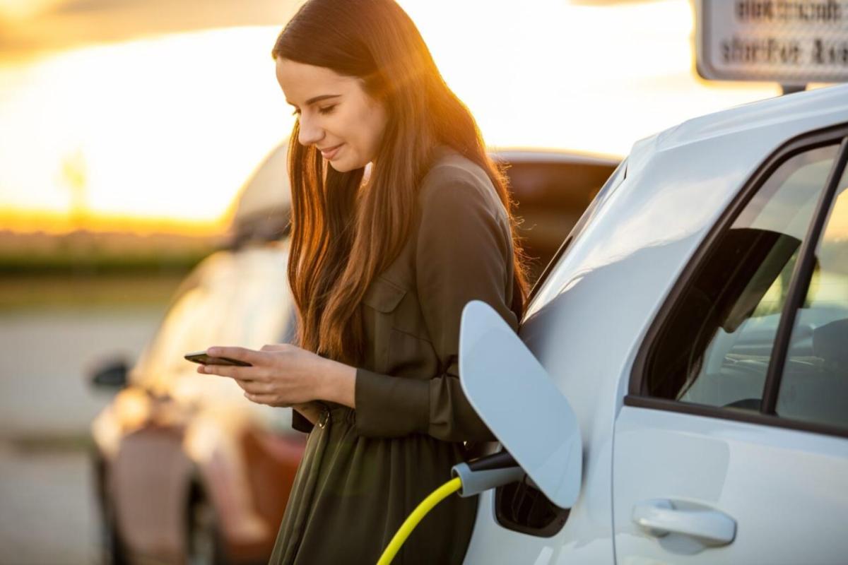 A person looking at their phone leaning on an EV plugged in.