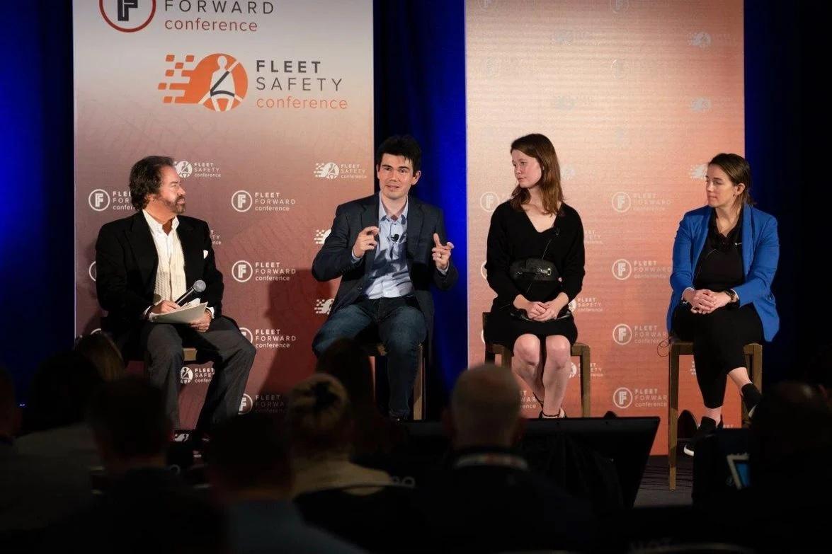 Frank Mycroft and the other panelists sit on stage in front of an orange backdrop.