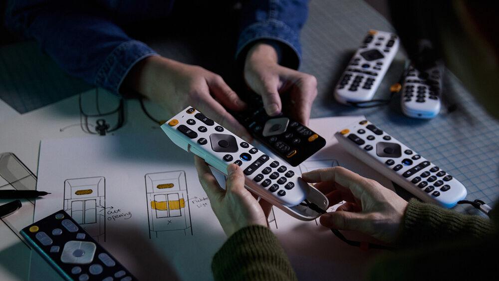 Two people holding different remotes next to each other over a table.