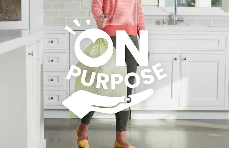 A person carrying a trash bag in a kitchen. "On Purpose" logo on top.