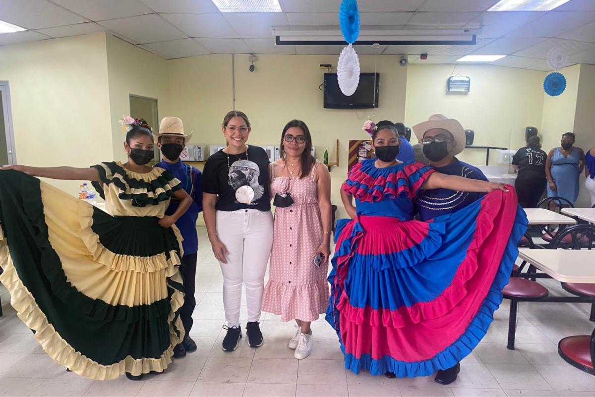 Dancers in colorful traditional dresses next to two employees in a lunch room