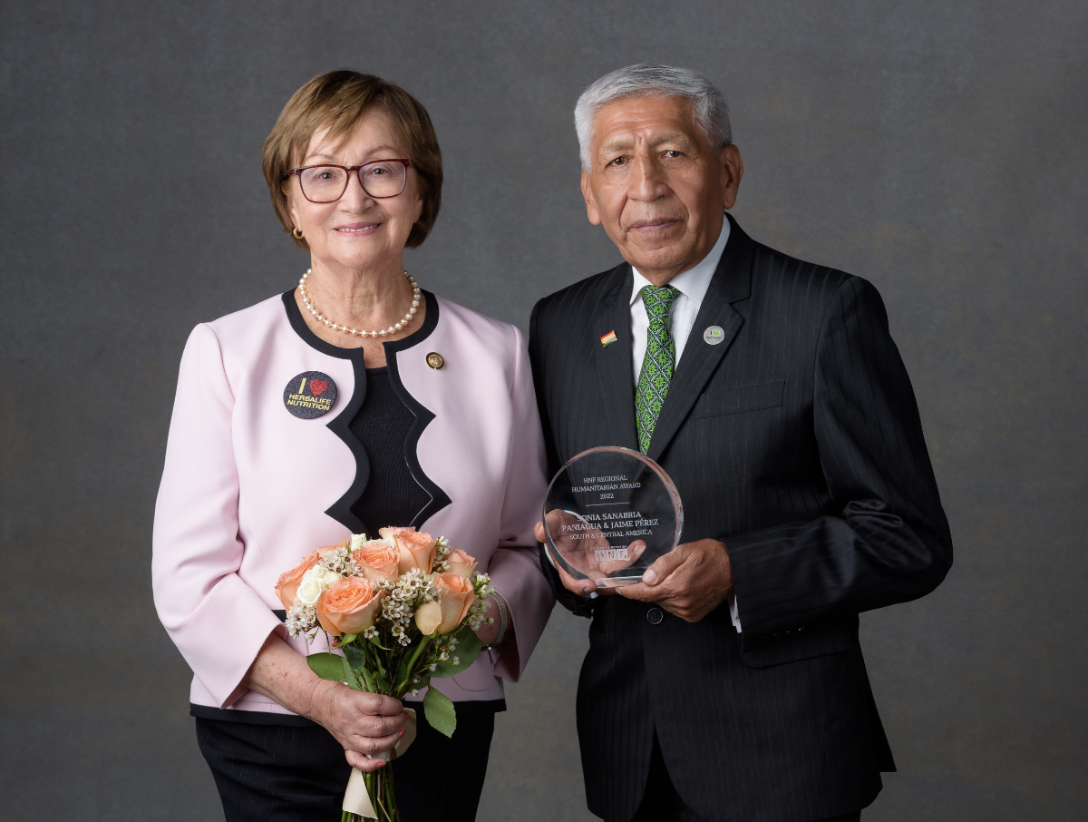 Two people stood next to each other smiling, one person holding flowers and the other holding an award