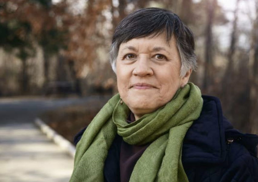 Person stood outside in front of trees, wearing a green scarf 