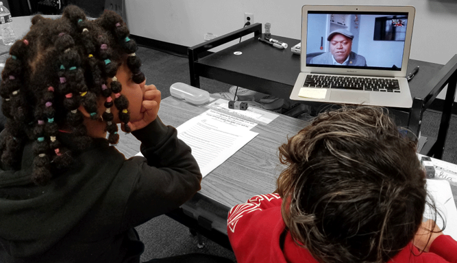 two students at a desk watch a video on a laptop