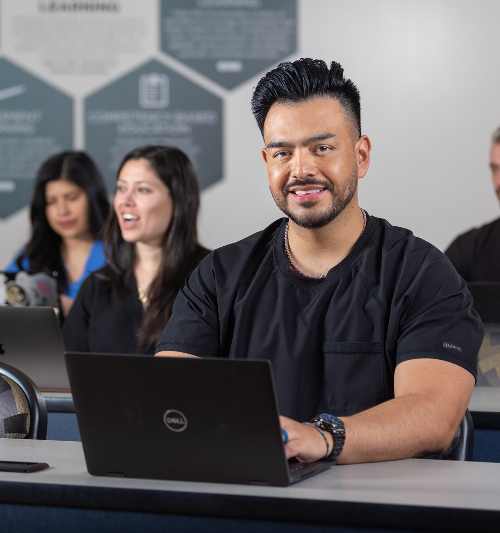 Juan Arbizu typing on a laptop in a classroom with others.