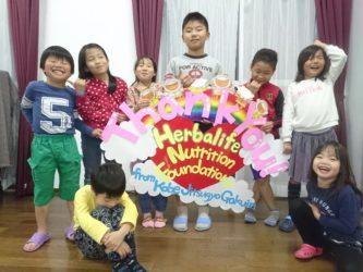 Children around a handmade sign reading Thank You Herbalife Nutrition Foundation