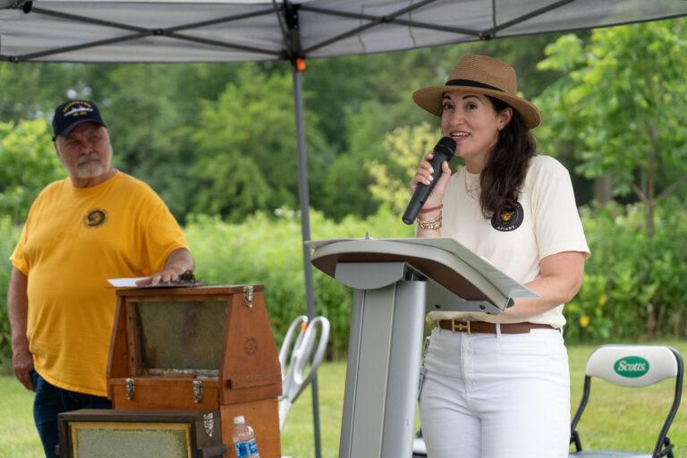 Katherine Dickens speaking at an outdoor podium.