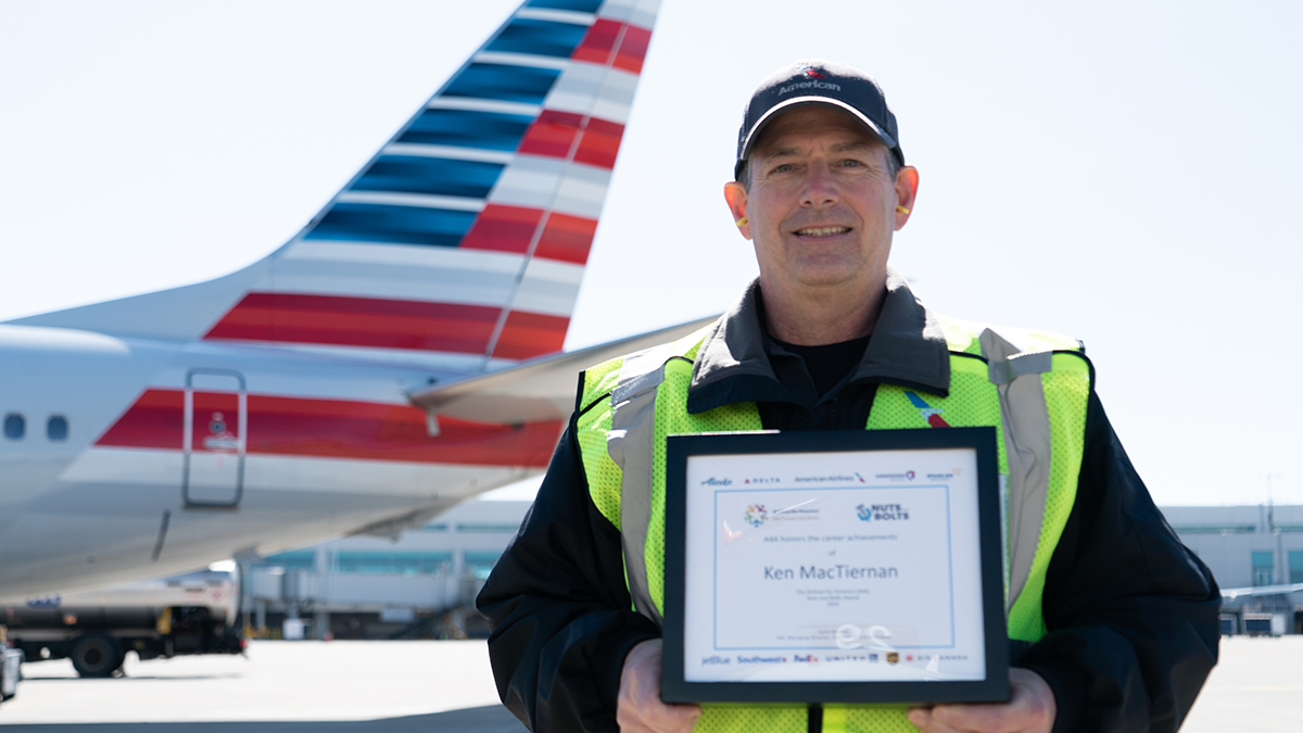 Ken MacTiernan holding a plaque outside, in front of an airplane.