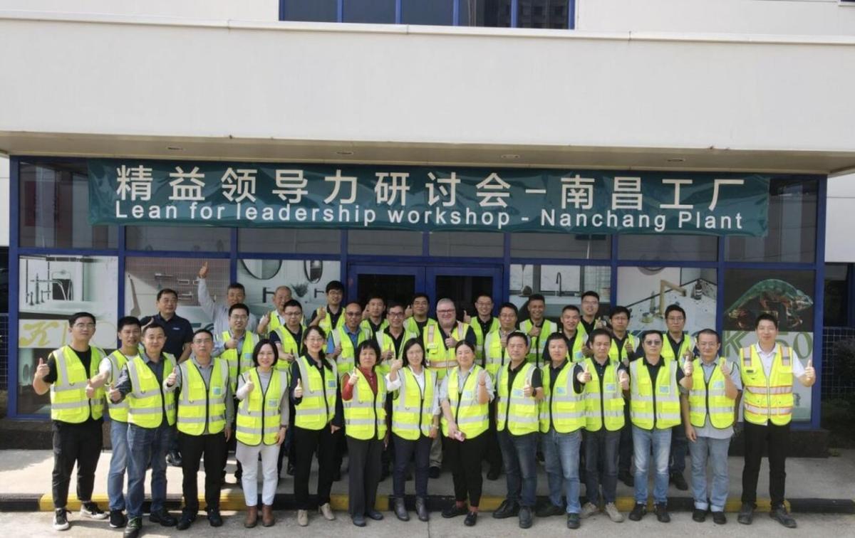 A group in front of a building, all wearing safety vests and giving 'thumbs-up'. A banner "Lean for leadership workshop - Nanchang Plant".