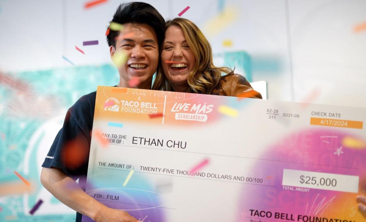 Two smiling people posed with a large check. Confetti falling around them.