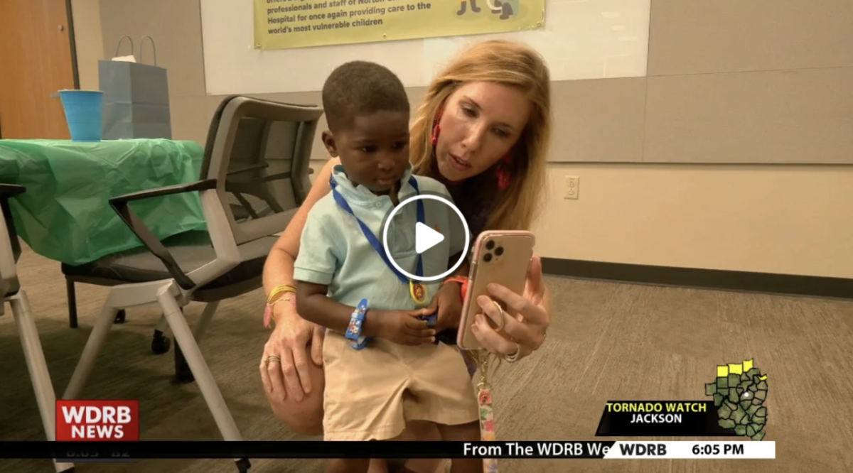 A woman holds up a phone for a child in a light green shirt