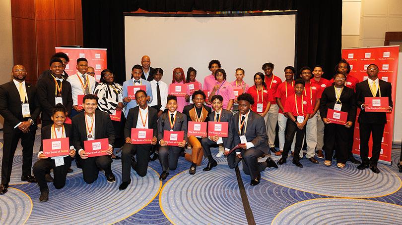 Group of young people standing together at a conference holding red Wells Fargo envelopes.